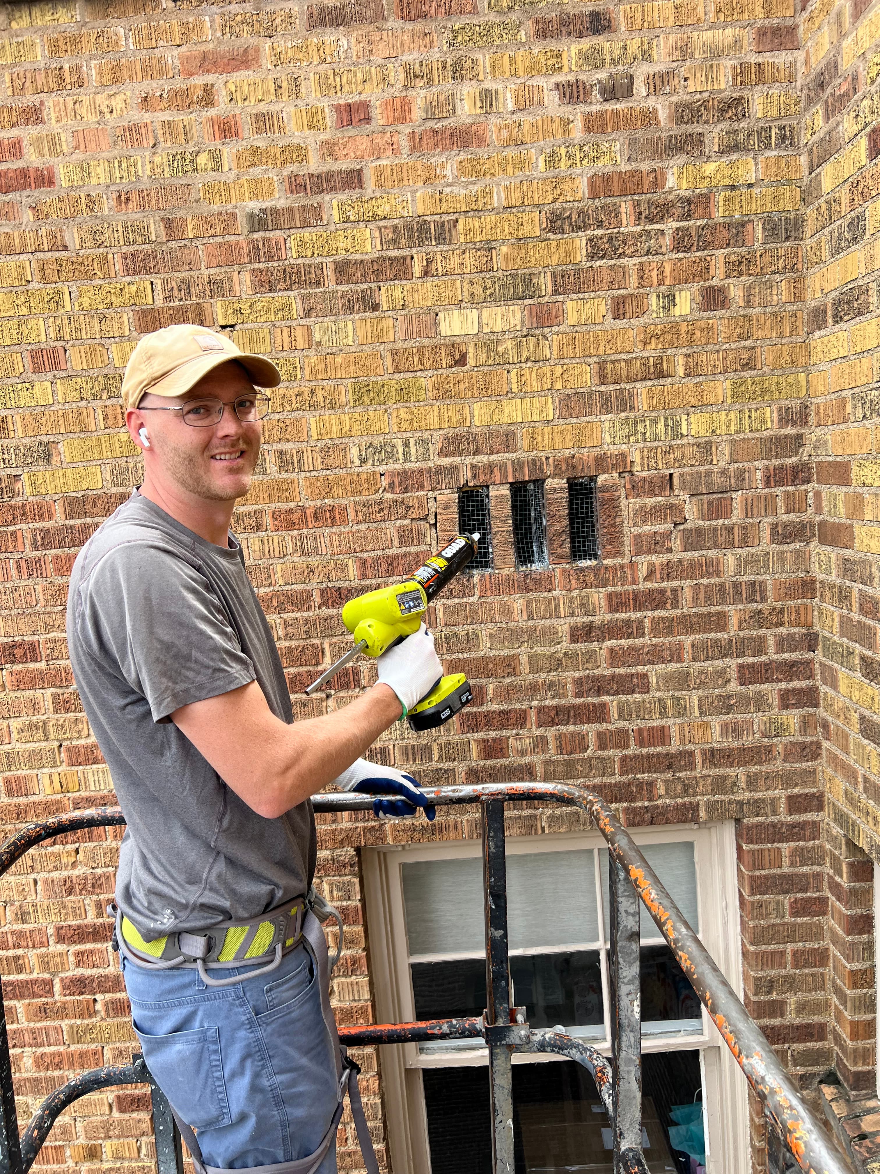 Technician on a lift sealing screened vents on a brick building